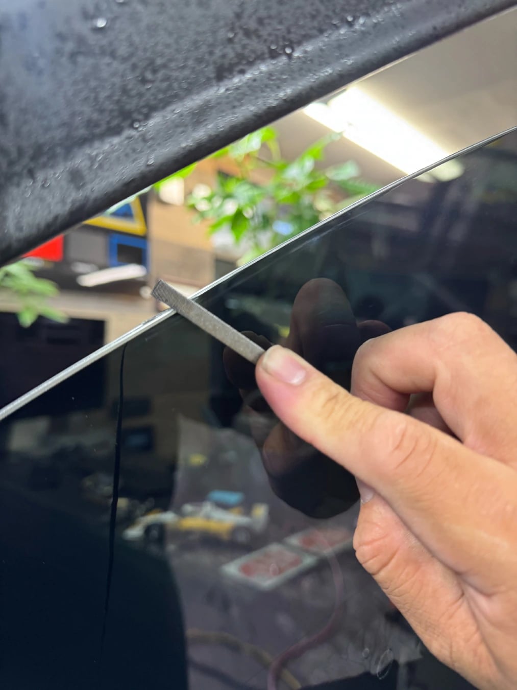 Hand finishing window tint along the top edge of a lowered door window at OC House of Tint